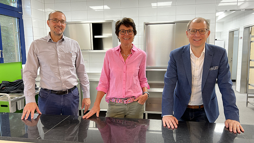 Drei Personen stehen in der Mensa hinter der Theke.