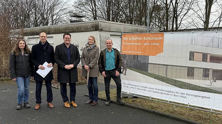 Vier Männer und Frauen vor einem Bauzaunbanner.