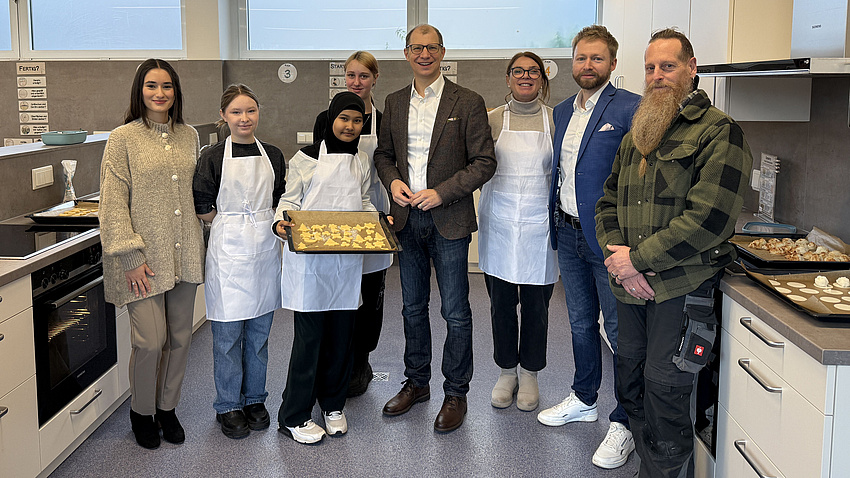 Landrat Jan Weckler, Schulleiter Marc Englert sowie Schülerinnen und Schüler. Sie stehen vor einer Küchenzeile.