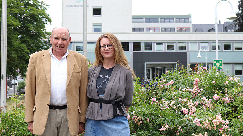 Ein Man und eine Frau stehen vor einem blühenden Rosenbusch.