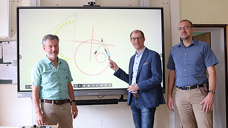 Drei Personen vor einer interaktiven, digitalen Schultafel.