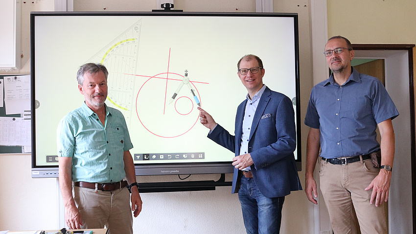 Drei Personen vor einer interaktiven, digitalen Schultafel.