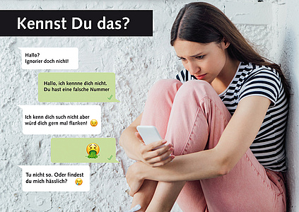 Junge Frau mit Handy in der Hand sitzt an einer Mauer