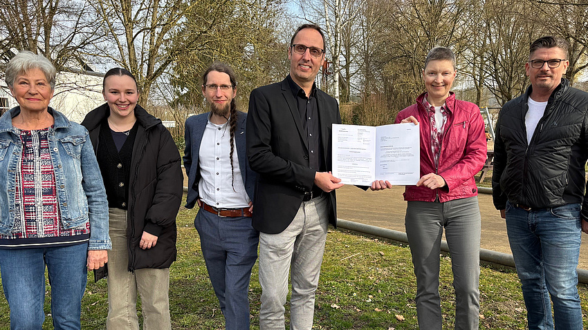 Sechs Personen schauen in die Kamera. Sie stehen in einem Park.