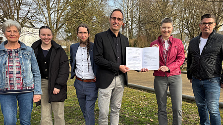 Sechs Personen schauen in die Kamera. Sie stehen in einem Park.
