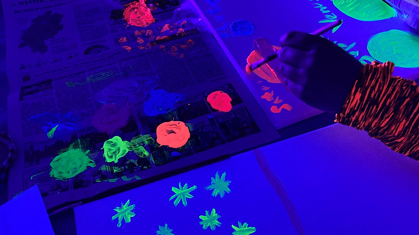 Jemand malt Blumen mit einem Pinsel und Far Schwarzlicht leuchtet