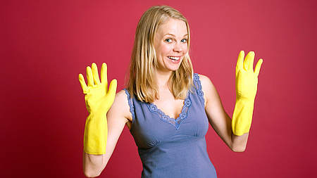 ein blonde Frau mit Gummihandschuhen, die Hände hält sie nach oben und lächelt