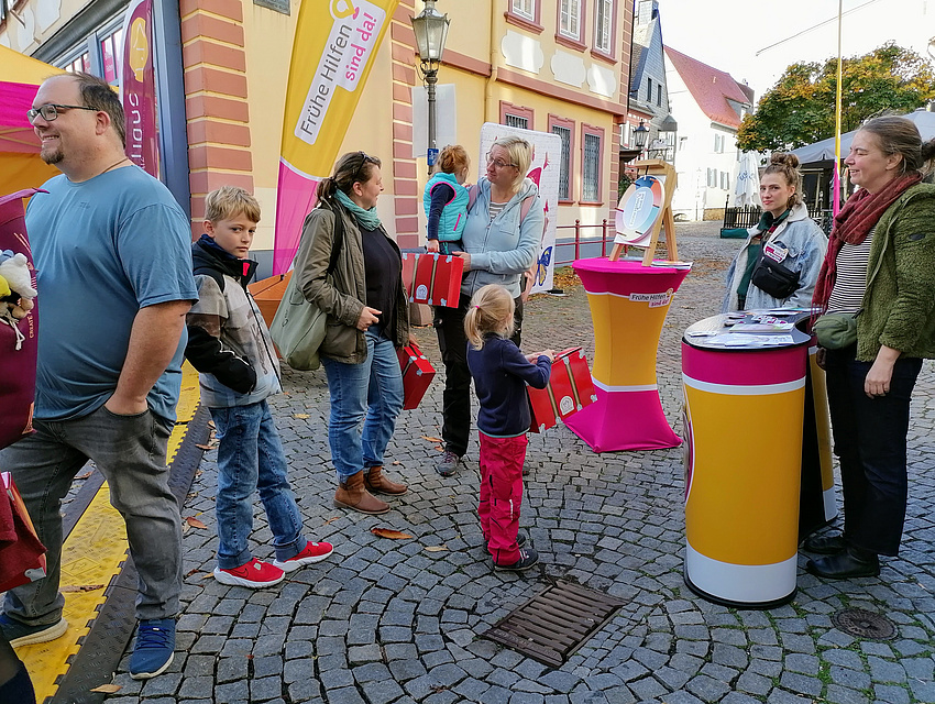 Mädchen mit rotem Koffer unterhält sich mit Erwachsenen
