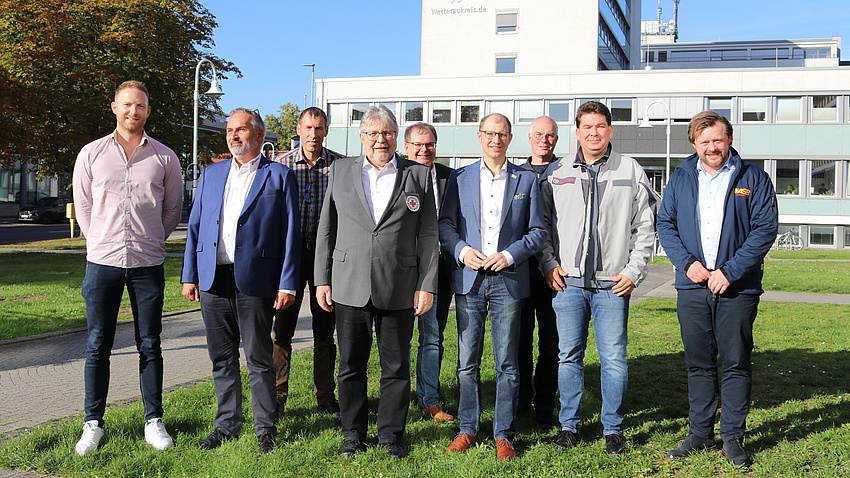 Mehrere Männer stehen auf einer kleinen Wiese. Im Hintergrund ein Baum und ein Gebäude.
