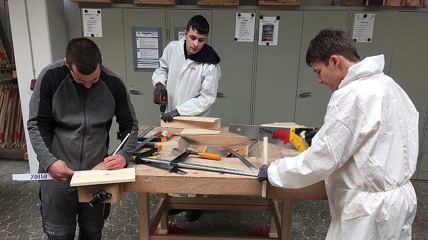 Drei Jugendliche arbeiten an einer Werkbank.