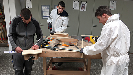 Drei Jungen arbeiten mit Werkzeugen an Holz.