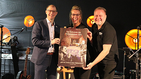 Der Landrat mit den Waldschmitts auf der Bühne. Corina Waldschmidt hält die Urkunde in der Hand.