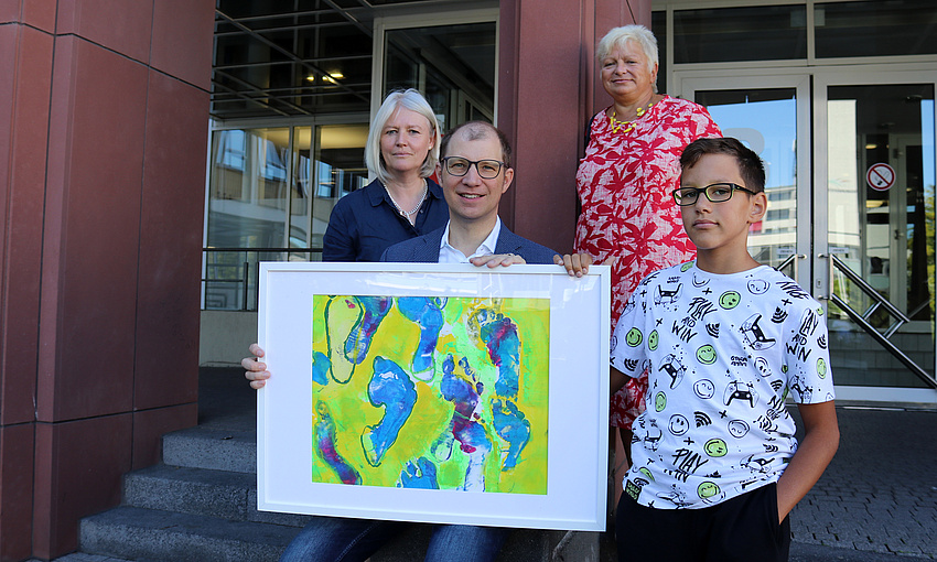 Ein Mann hält ein großformatiges Bild in der Hand. Neben ihm steht ein Junge, hinter ihm stehen zwei Frauen.