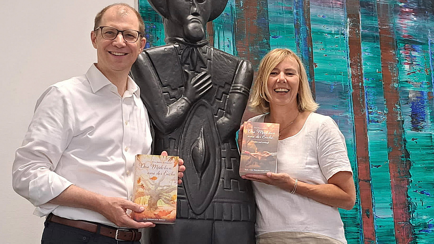 Ein Mann und eine Frau stehen neben einer Statue, die den Keltenfürsten vom Glauberg darstellen soll. Im Hintergrund ein abstraktes Gemälde