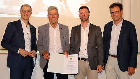 Vier Männer halten eine Urkunde in die Kamera.