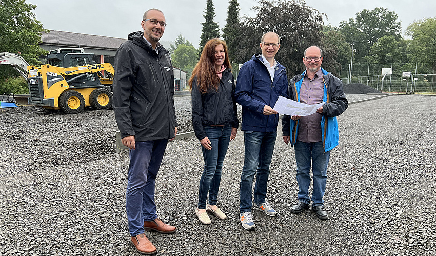 Die vier Personen stehen auf einem Schotterfeld.