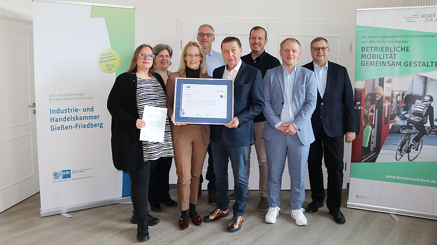 Eine Gruppe von Leuten. Zwei von ihnen halten eine eingerahmte Urkunde.