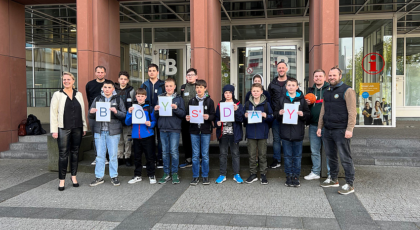 Eine Jungengruppe steht vor der Treppe zu einem Gebäude. Rechts und links neben den Jugendlichen stehen Erwachsene.