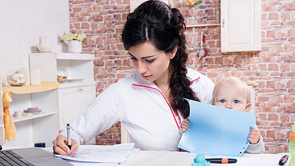 Junge Mutter mit kleinem Kind auf dem Arbeit versucht gleichzeitig zu arbeiten.