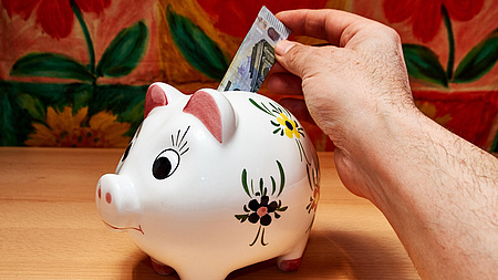 Eine Hand schiebt einen Geldschein in ein Sparschwein.