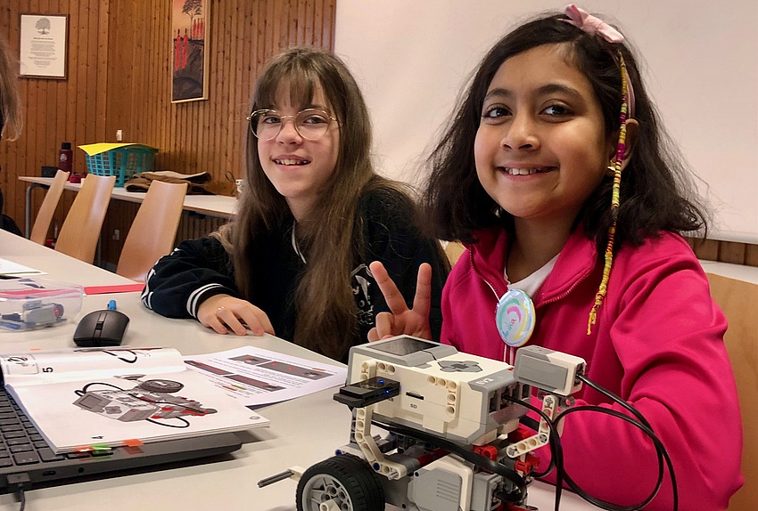 Zwei Mädchen an einem Tisch mit einem kleinen Roboter auf Rädern