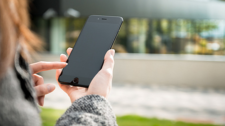 Zu sehen ist eine Hand und das Seitenprofil einer Frau, die ein Handy hält.