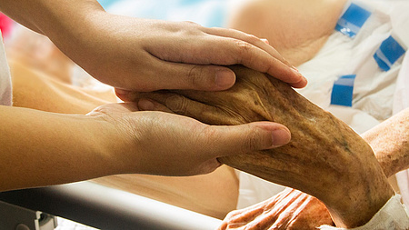 Eine alte, gebrechliche Hand wird von zwei jungen Händen gehalten.