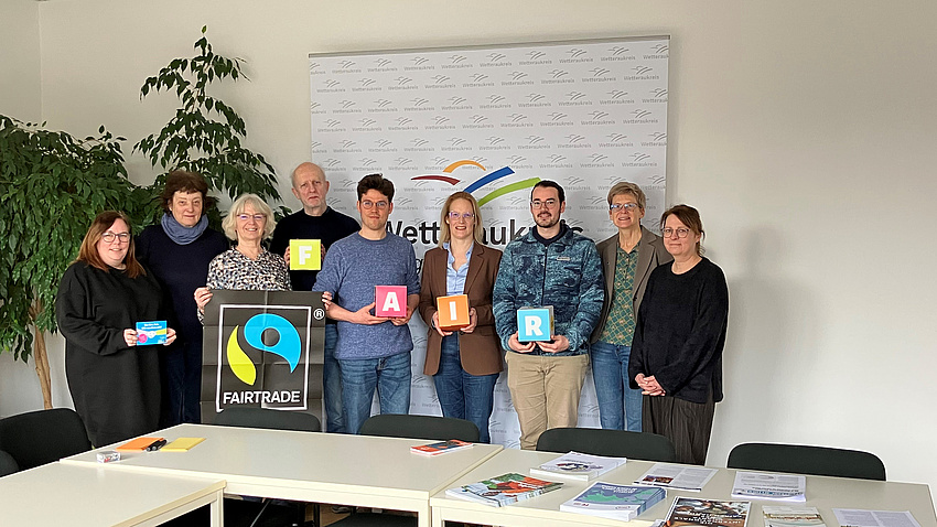 Eine Gruppe von Menschen steht zusammen und präsentiert verschiedene Logos und Broschüren zum Thema Fair-Trade