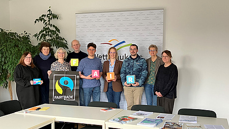 Eine Gruppe von Menschen steht zusammen und präsentiert verschiedene Logos und Broschüren zum Thema Fair-Trade