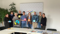 Eine Gruppe von Menschen steht zusammen und präsentiert verschiedene Logos und Broschüren zum Thema Fair-Trade