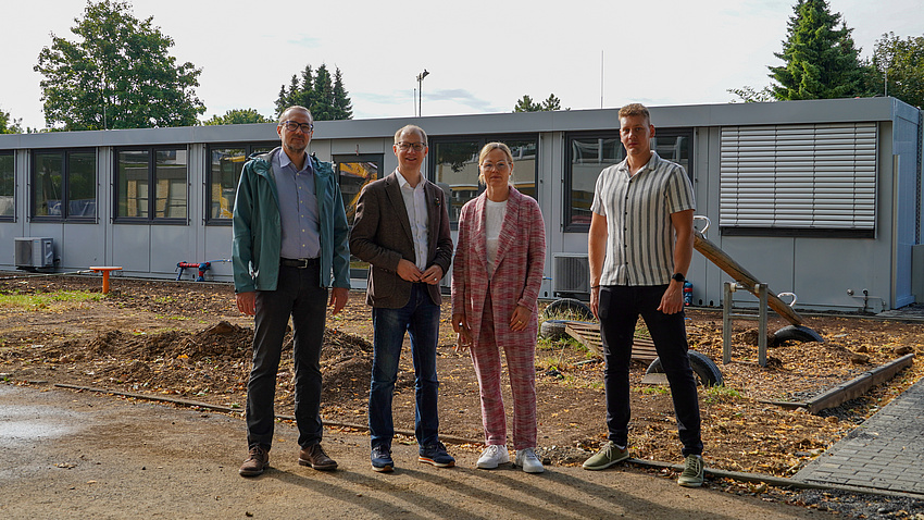Vier Personen stehen vor einem einstöckigen Gebäude.