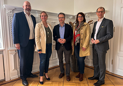 Zwei Frauen und drei Männer stehen nebeneinander und lächeln in die Kamera.