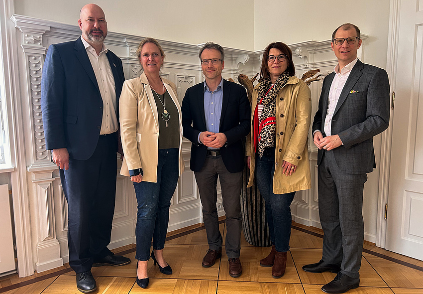 Zwei Frauen und drei Männer stehen nebeneinander und lächeln in die Kamera.