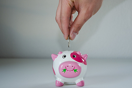 Eine Hand steckt von oben eine Münze in ein Sparschwein.