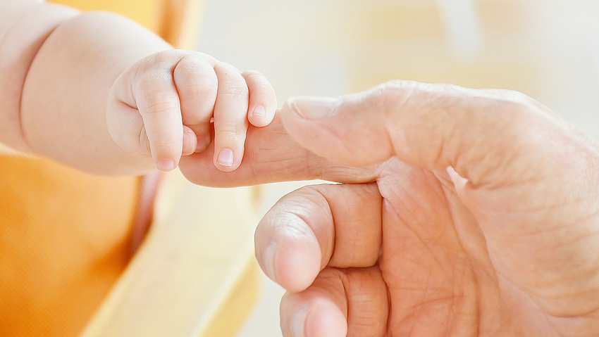 Eine erwachsene Hand und eine Babyhand berühren sich.