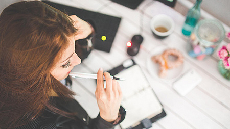 Ein Frau hat einen Terminkalender vor sich und einen Stift in der Hand und überlegt.