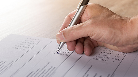 Eine Hand hält einen Stift und füllt einen Fragebogen aus.