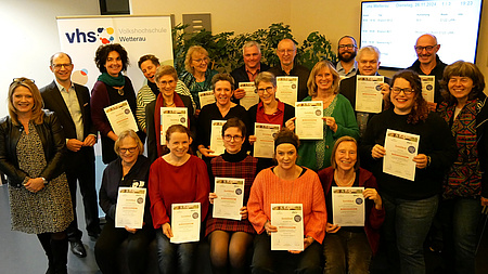 Eine Gruppe von vielen fröhlichen Menschen hält stolz Zertifikate in der Hand.