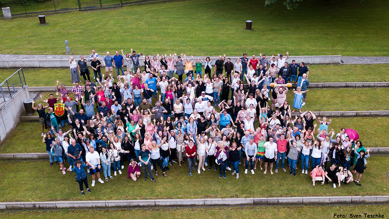 Beschäftigte der Stadtverwaltung Büdingen stehen auf einer Wiese im Büdingen Freibad und winken lächelnd auf die Kamera zu.