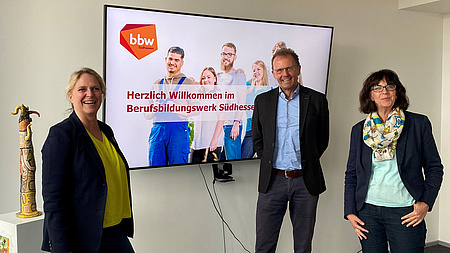 Zwei Frauen und ein Mann lächeln in die Kamera. Im Hintergrund ein Whiteboard. Auf diesem steht: Herzlich willkommen im Berufsbildungswerk Südhessen.