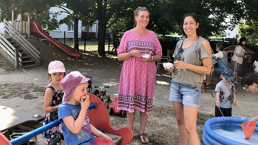 Zwei junge Mütter mit Kindern auf einem Spielplatz.
