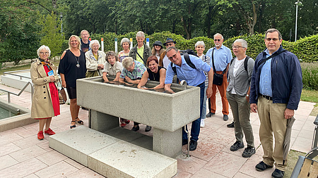 Mehrere Personen stehen um ein Kneippbecken für Armbäder. Vier Personen tauchen ihre Arme ins Wasser.