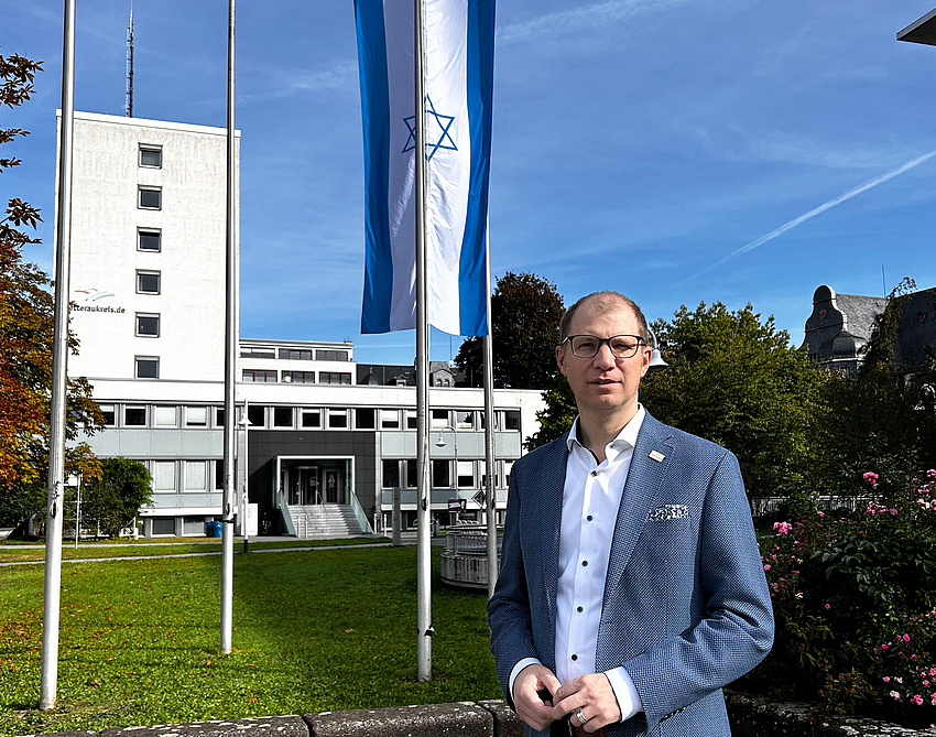 Ein Mann steht auf einem freien Platz. Im Hintergrund weht die israelische Flagge