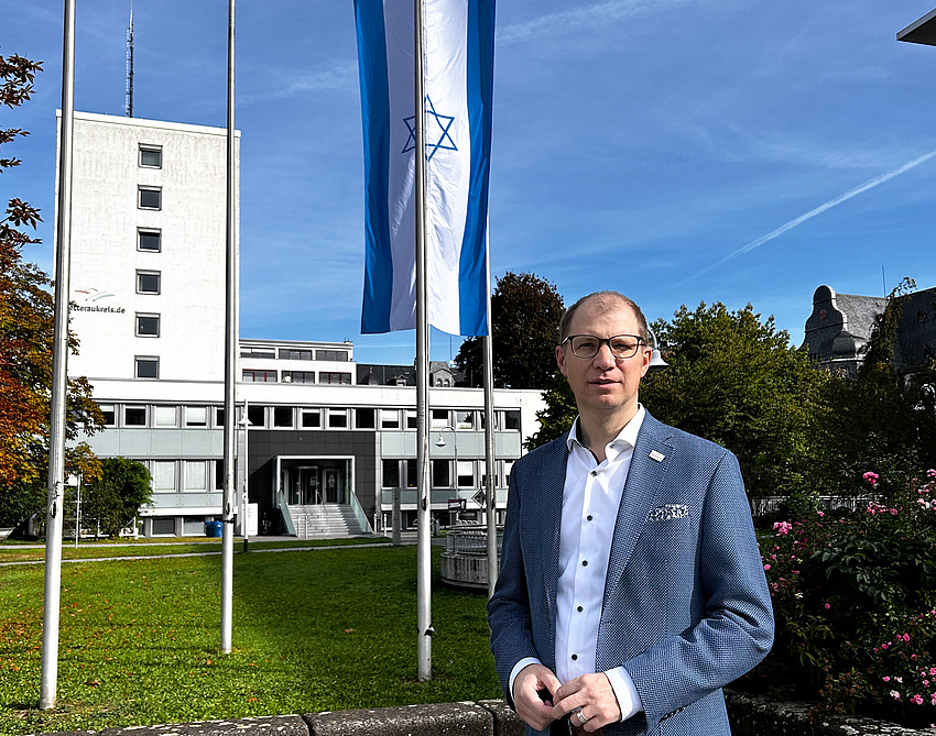 Ein Mann steht auf einem freien Platz. Im Hintergrund weht die israelische Flagge