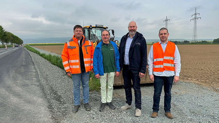 Vier Männer stehen am geschotterten Seitenbankett einer Straße