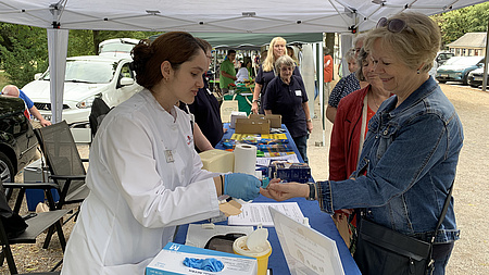 Eine junge Frau im Apothekerkittel nimmt einer Besucherin Blut ab.