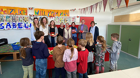 Mehrere Frauen stehen gegenüber einer kleinen Schulklasse von Grundschülern.