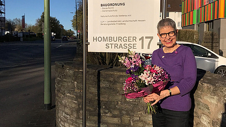 Eine Frau steht an einer Straße und hält einen Blumenstrauß in den Händen.