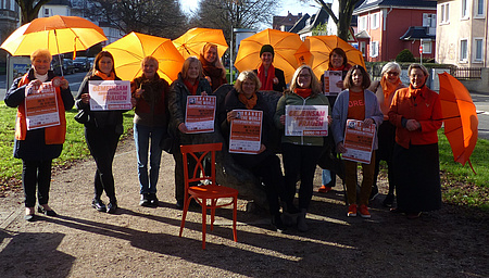 Zu sehen ist eine Gruppe von Frauen mit orangefarbenen Regenschirmen und Plakaten.