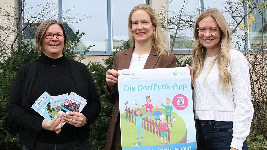 Ehrenamtskoordinatorin Anita Graf, Erste Kreisbeigeordnete Birgit Weckler und Antonia Klein vom Fachdienst Kreisentwicklung zeigen ein Plakat. Darauf steht "DorfFunk".